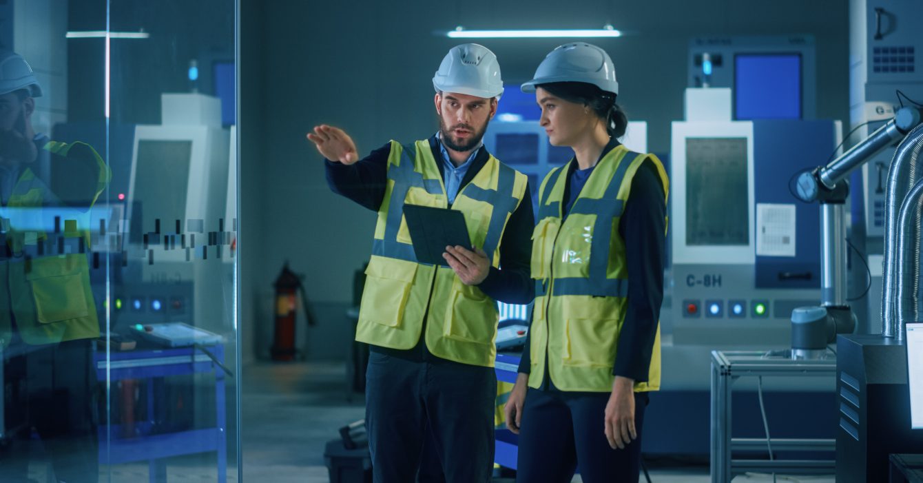 Modern,Factory:,Female,And,Male,Engineers,Wearing,Safety,Jackets,,Hardhats